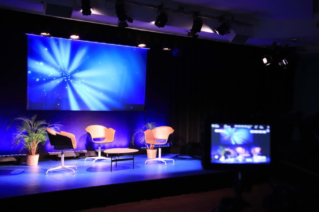Blue light, three chairs and a small table: The podium is ready in the event hall