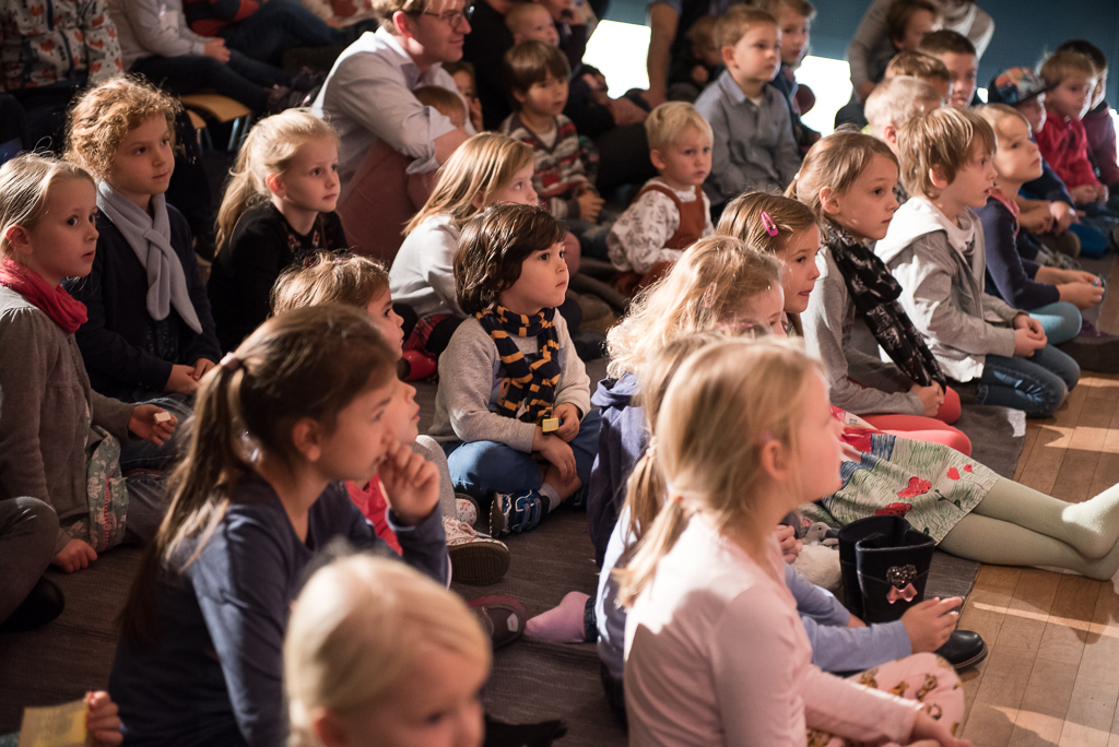 Many children sit excitedly on the floor, listening to the music and singing of Marko Simsa in the House of Music