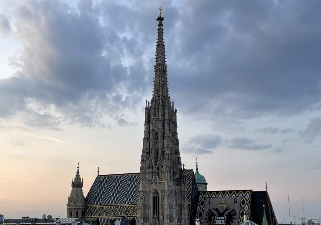 Der Stephansdom in Wien mit seinem hohen Südturm und dem bunten Ziegeldach mit Mustern und Wappen, aufgenommen bei bewölktem Himmel in der Abenddämmerung.