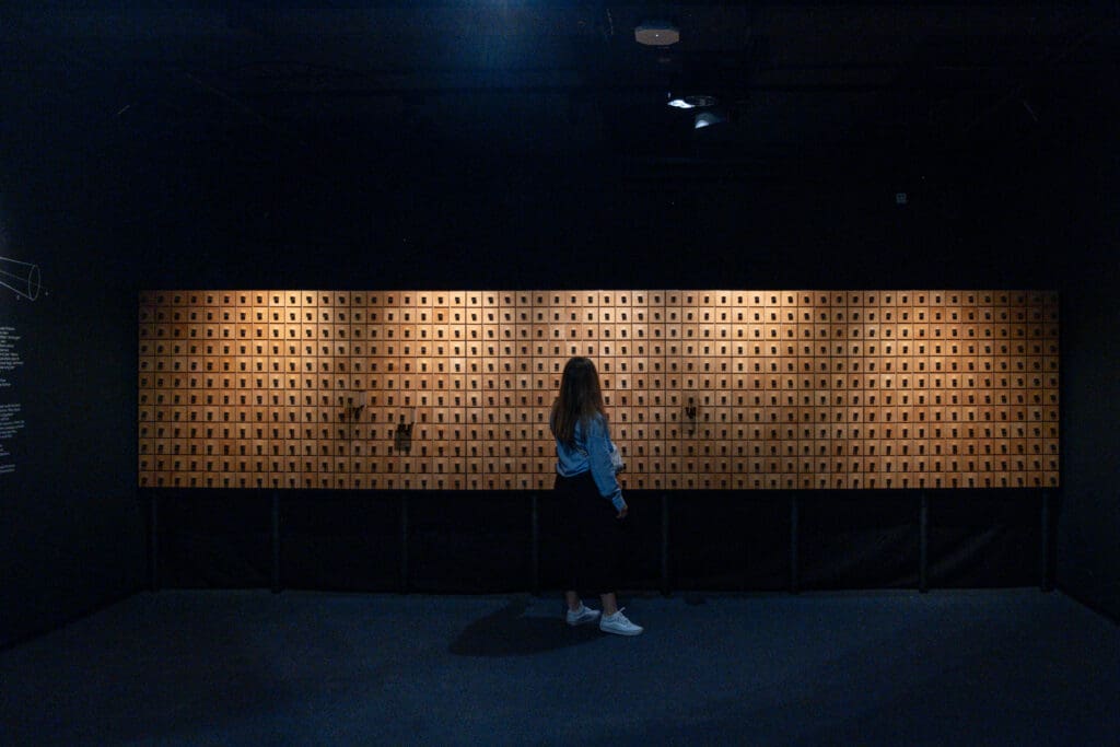 Frau steht in einem dunklen Raum vor einer großen beleuchteten Wand mit vielen kleinen quadratischen Fächern.